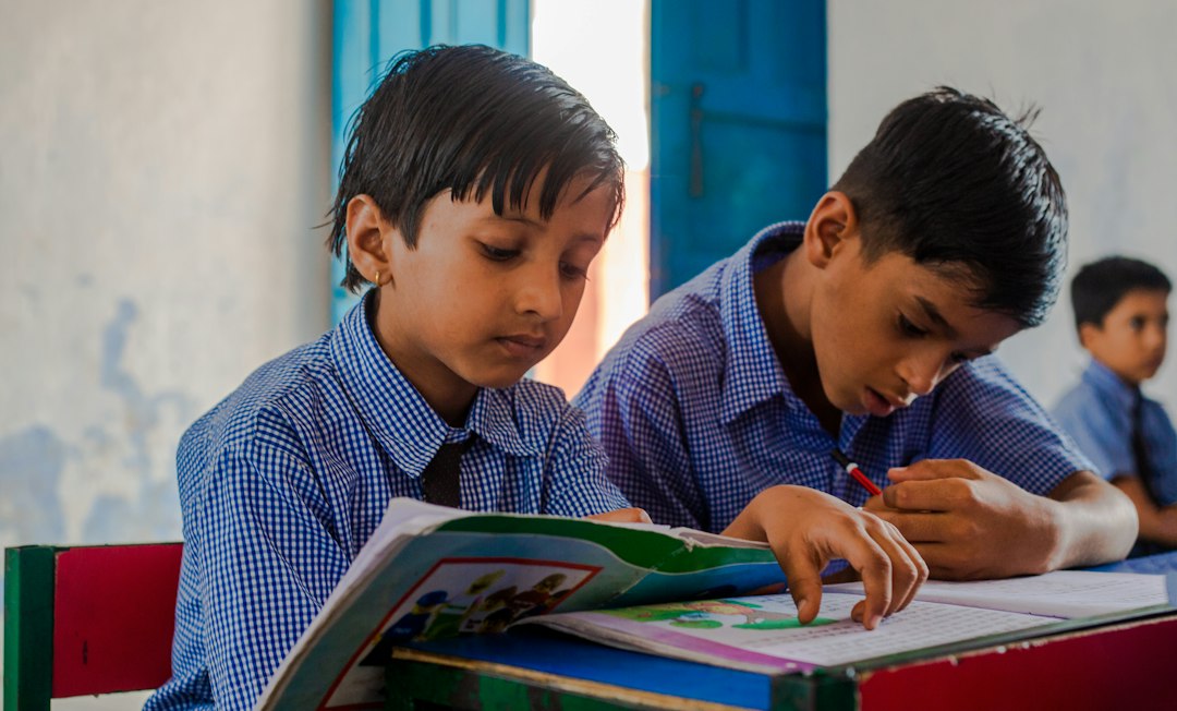 two young boys sitting at a desk with a book